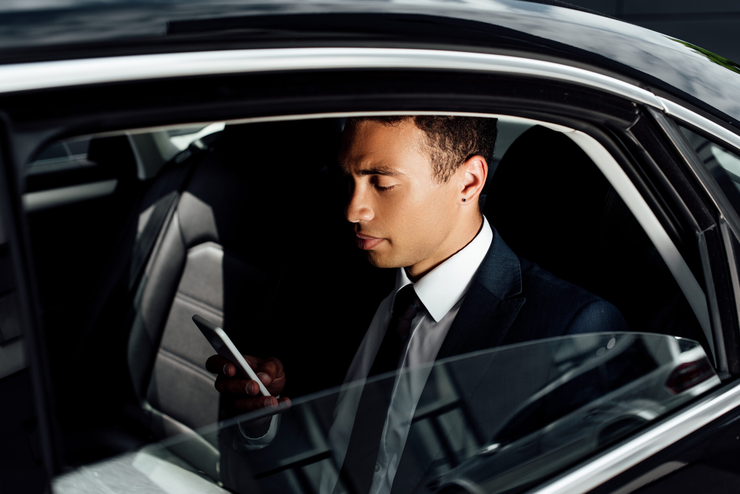 african american businessman in suit using smartphone in car