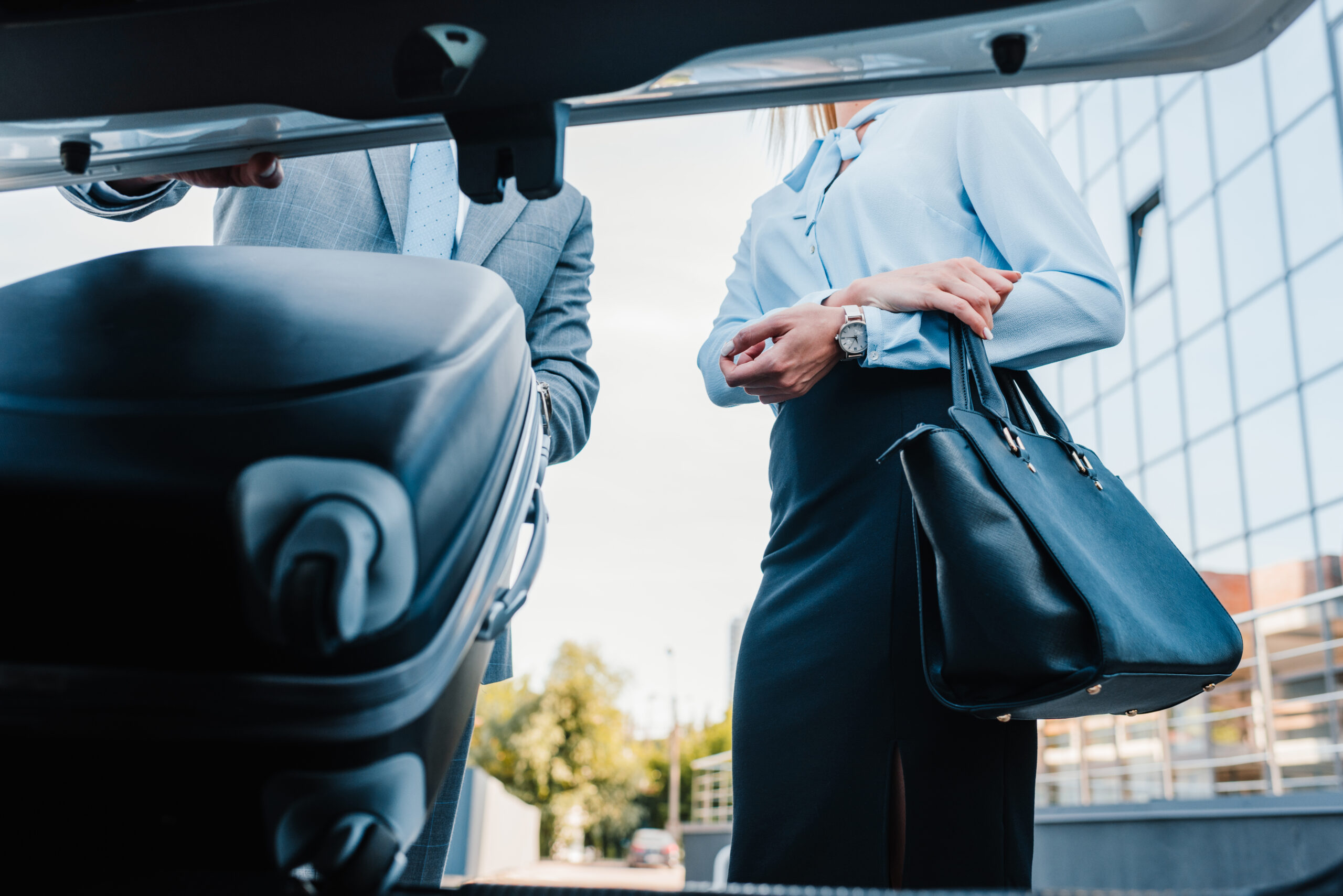 partial view of businessman putting baggage into car with colleague near by